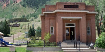 Exterior of the Silverton Public Library built in 1906 and the Christ of the Mines Shrine in the background on the left