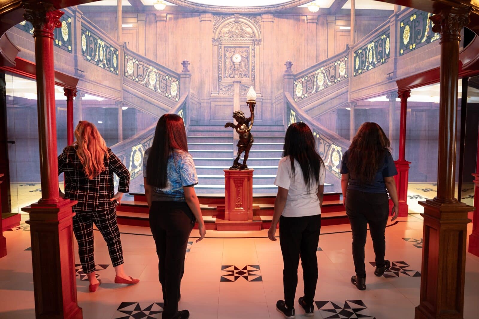 Four women stand in front of a sculpture and a grand staircase display of the Titanic