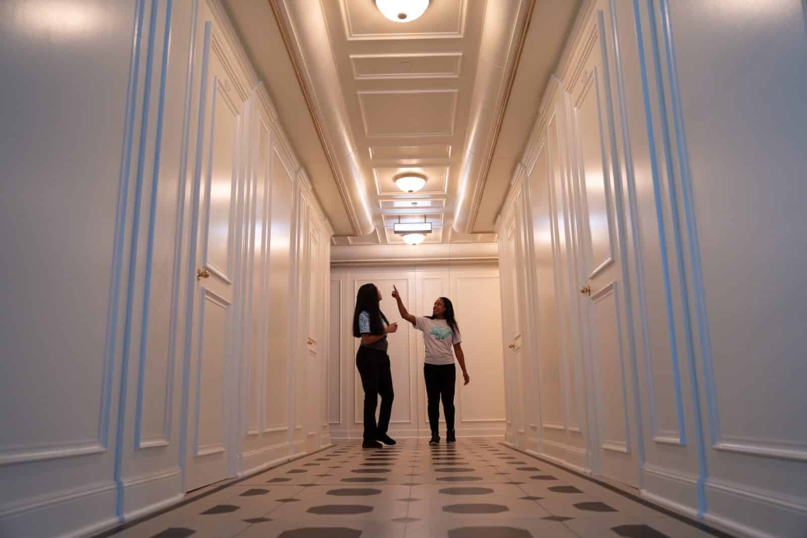 Women stand in a white hallway set of the Titantic